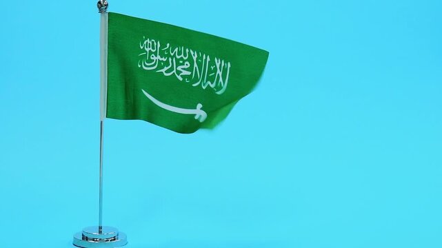 Slow motion video of Saudi Arabia table flag on blue background