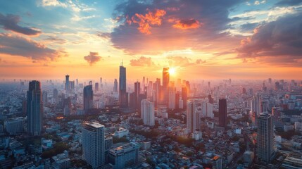 Obraz premium A panoramic shot of a city skyline with the sun setting behind high-rise buildings, casting a warm, colorful glow over the cityscape.