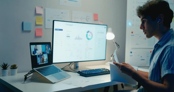 Young Asia male use laptop talk to colleague plan in video call meeting on desk in living room at home office overtime night. Work from house, financial plan, digital nomad job and Gen Z talent.