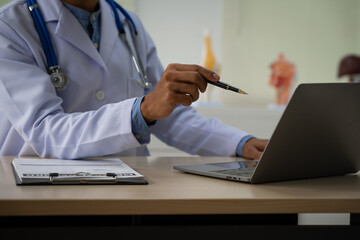 A male doctor sits at a desk in the heart clinic, consulting online and giving advice. The vascular surgery clinic offers an electrocardiogram service with modern technology and expert care.