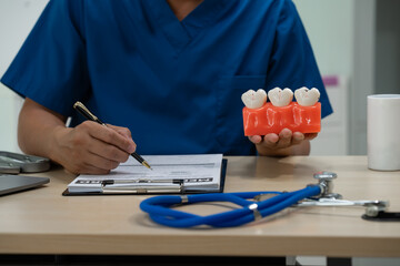 A male doctor sits working at the table in a dentist's clinic, explaining tooth decay, wisdom...