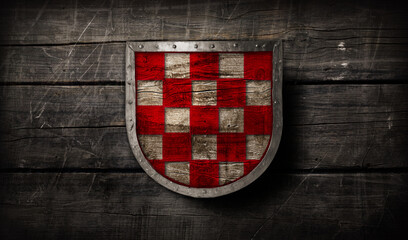 Medieval wooden shield with silver brim and red checkered pattern design on ancient wooden background