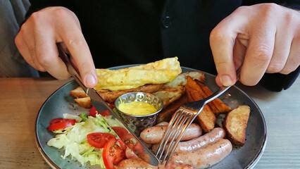 Man Eating Sausages and Potato Wedges with Fork and Knife