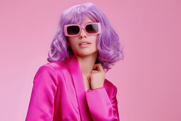 Purplehaired woman in sunglasses and a pink suit, posing confidently against a matching pink...