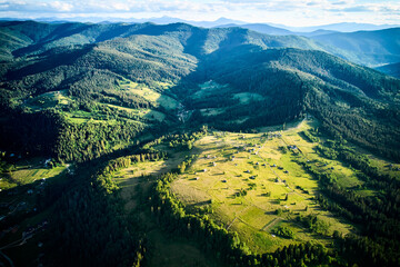 Aerial view of sunlit valley, dotted with small houses and winding roads, surrounded by dense...