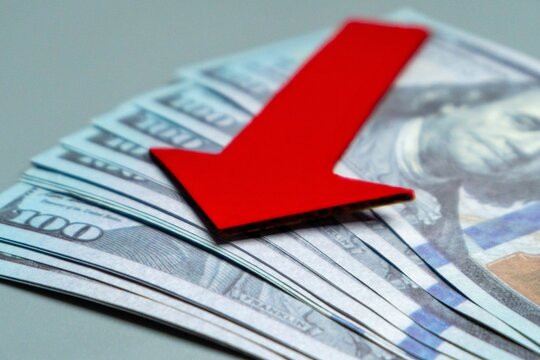 A red arrow pointing downwards on top of a pile of US dollar bills. Economic recession, financial decline, economic downturn concept.