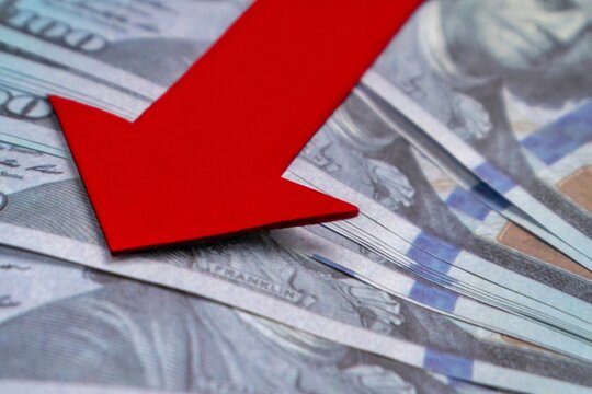 A red arrow pointing downwards on top of a pile of US dollar bills. Economic recession, financial decline, economic downturn concept.