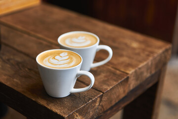 Two cups of hot coffee with milk on a wooden table outside