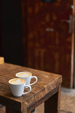 Two cups of hot coffee with milk on a wooden table outside