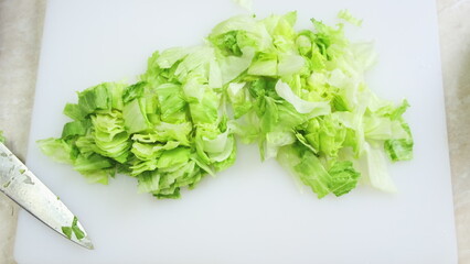 Fresh iceberg salad cutting close up on white kitchen board. Chef hands in blue gloves mince green...