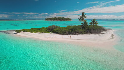 Woman walks alone on a desert island with turquoise sea and palm trees swaying, a message help in the sand adds mystery to this tranquil paradise