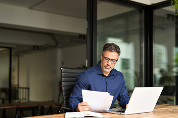 Senior mature male account bank manager executive working on laptop checking paper financial report...