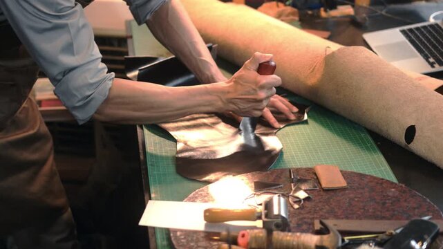 Slow motion shot of craftsman cutting brown leather patterns in atelier workshop. Handmade concept