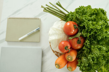 Top view of fresh vegetables preparing for salad with laptop and notebook on table