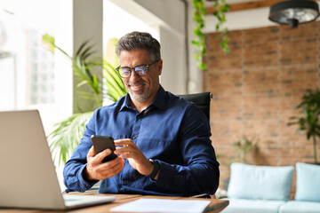 Happy middle aged businessman using mobile phone working in office. Busy smiling 50 years old man executive holding smartphone technology looking at cellphone making bank transaction payment in app. - Powered by Adobe