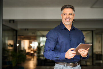 Middle aged happy business man professional manager executive standing in office using tablet...
