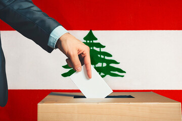 A hand holds a ballot in a ballot box against the background of the Lebanese flag. People place...