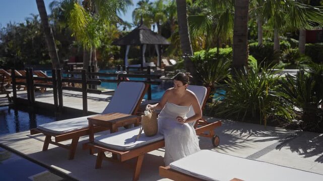 A beautiful young woman relaxes on a sun lounger at a luxurious bali hotel, showcasing the serene tropical resort ambiance.