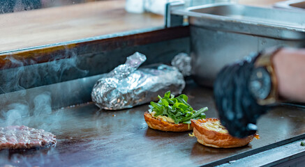 Someone is making a burger with beef, salad and other ingredients at a food stall in the marketplace.