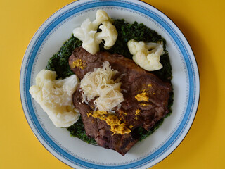 A juicy T-Bone steak on a bed of chopped spinach with cauliflower sauerkraut and Australian mustard.