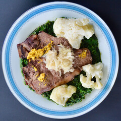 A juicy T-Bone steak on a bed of chopped spinach with cauliflower sauerkraut and Australian mustard.