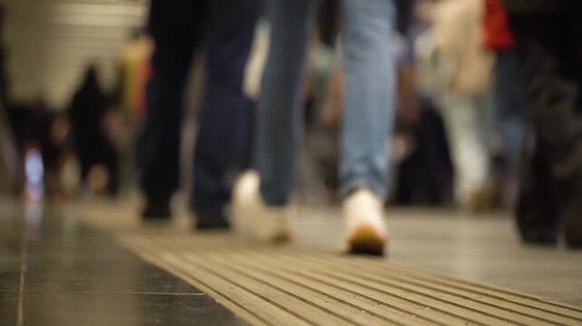 Crowd of unrecognizable pedestrians walks through the underpass city. Low angle view of legs and feet of people. Society and city life concept. 4K
