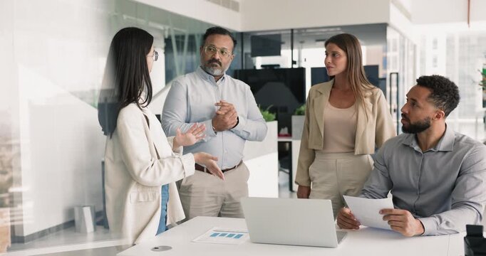 Multiethnic employees listening speech of young European teammate, take part in group meeting briefing gathered in modern office for opinion exchange, reviewing new project details, decision-making