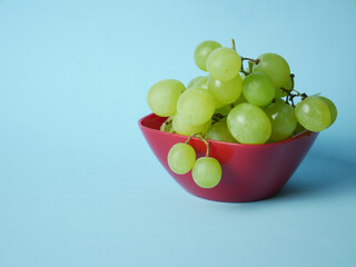 Grapes in the red bowl on the blue background.