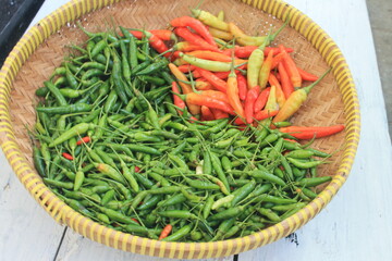 Red cayenne pepper and green cayenne pepper in a woven bamboo container on a wooden table

