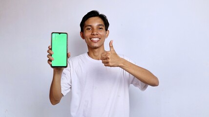 smiling asian young man wearing white shirt showing green screen mobile phone and ok gesture for advertising