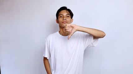 Asian young man wearing white shirt gesturing thumbs down