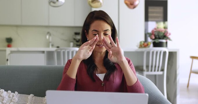 Attractive Latina woman sit on couch using laptop take part in video call with family, friend, getting professional counseling advice, share thoughts, looks interested in remote communication at home