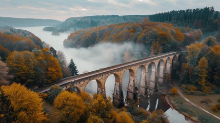 A train crosses an old, fog-covered bridge with autumn trees and gray skies, creating a serene and nostalgic scene. The setting exudes mystery and charm, encapsulating the essence of fall.