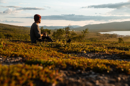 Young white man eating a delicious meal, enjoying the view over Padjelanta National Park in Swedish Lapland during golden hour. Close to Padjelantaleden Kisuris.