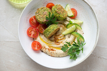 Hummus with paprika, falafel, fresh tomatoes and cucumber in a beige plate, horizontal shot, middle closeup, elevated view