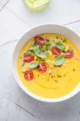 Bowl of chilled gazpacho with sweet corn and yellow tomatoes, vertical shot on a white granite background, elevated view