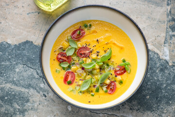 Bowl of sweet corn and yellow tomatoes gazpacho, horizontal shot on a grey and beige granite background, high angle view
