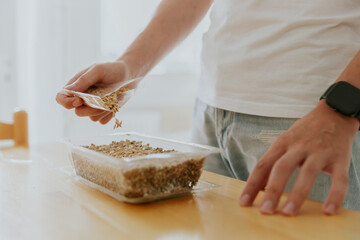 A young man plants wheat seeds in a container.