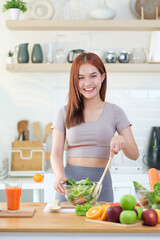 A young woman in athletic wear smiles brightly while preparing a fresh salad in a stylish, modern kitchen.