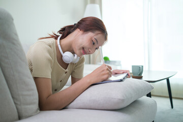A young woman is deeply engrossed in her studies, using a tablet and stylus while lying on a light...