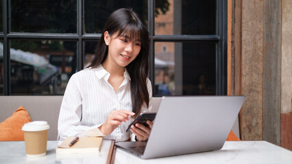 Business woman is seated at an outdoor café table, smiling as she looks at her smartphone.