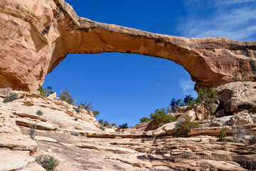 Stunning low view of Owachomo Bridge from below, located in Natural Bridges National Monument, Utah. The photo captures the impressive natural rock arch framed by clear blue skies - USA