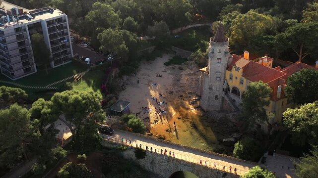 Drone capturing Condes de Castro Guimaraes museum and trees during sunny day. From above of historic building surrounded with lush forest at Cascais, Portugal.