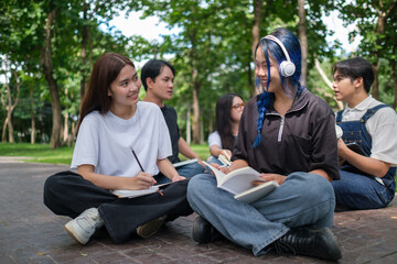 A group of diverse young students sits together outdoors in a park, engaging in a collaborative study session.
