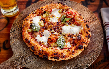 Vegetarian thick crust pizza on a round wooden cutting board with a beer on the side