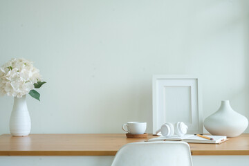 Empty picture frame, coffee cup, headphone and ceramic vase on wooden table.