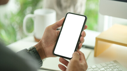 Close up view of man hands holding smart phone over working desk. Blank screen for your advertise design.