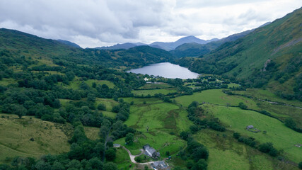 beautiful aerial shot of a green valley with a tranquil lake in the center, surrounded by rolling hills and forests, with a cloudy sky above.