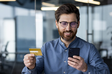 Close-up photo of smiling young business man sitting in modern office wearing glasses and blue...