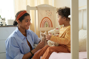 Obraz premium Smiling mother giving teddy bear to her delighted young son in cozy child bedroom. Interacting with toys, creating an atmosphere of warmth and joy